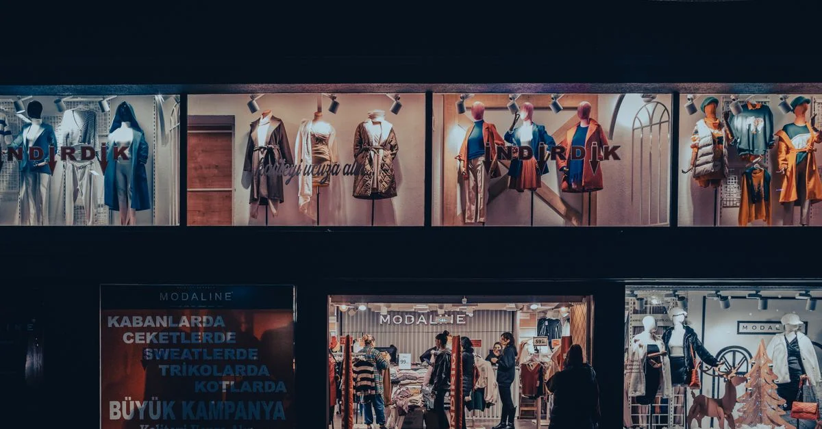 Vitrine de magasin de mode éclairée avec des mannequins et un éclairage dramatique la nuit.