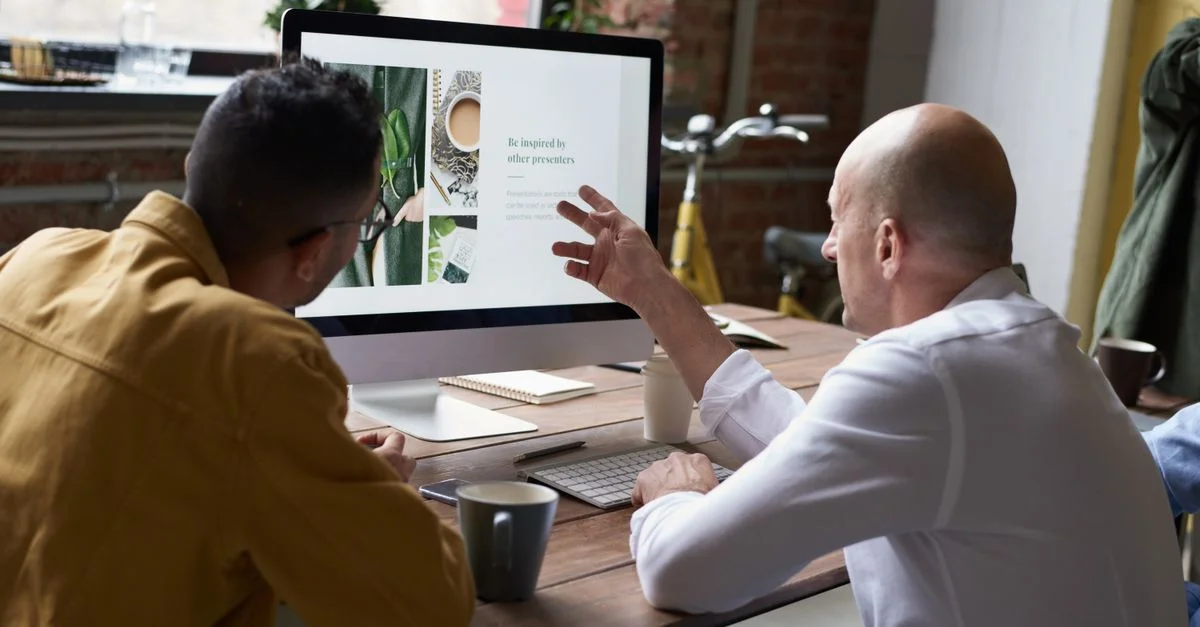 Deux collègues collaborant sur un projet dans un bureau moderne avec un écran d'ordinateur et du café.