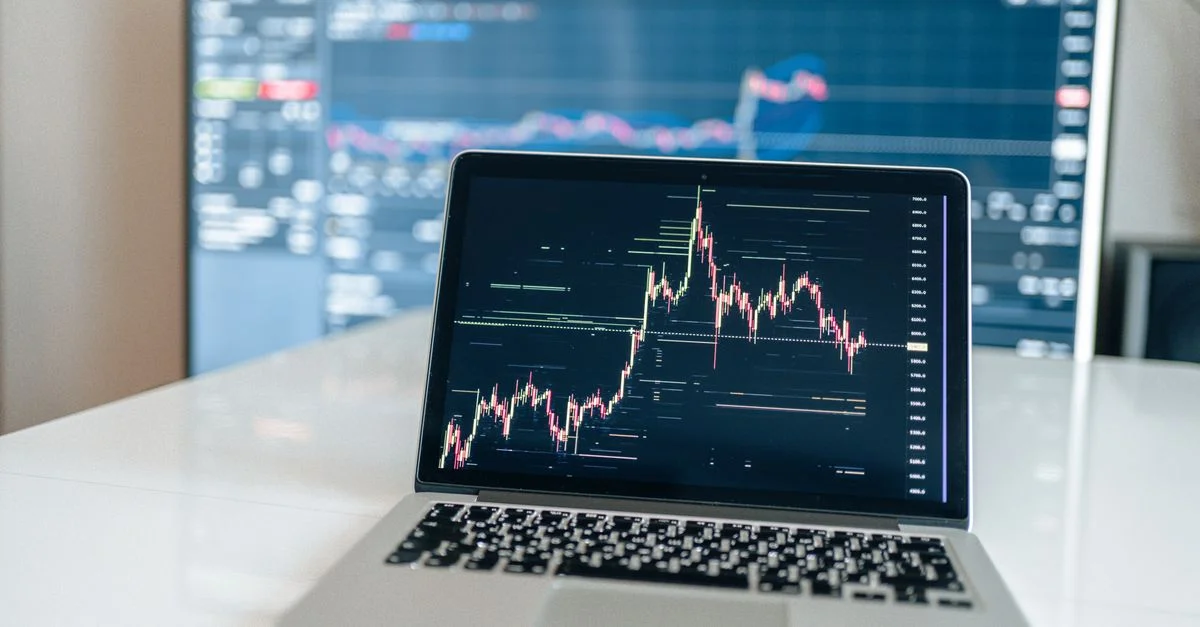 Ordinateur portable affichant un graphique de trading de cryptomonnaie sur un bureau blanc.
