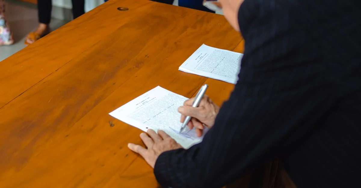 Gros plan d'un homme d'affaires signant des documents officiels à un bureau en bois.