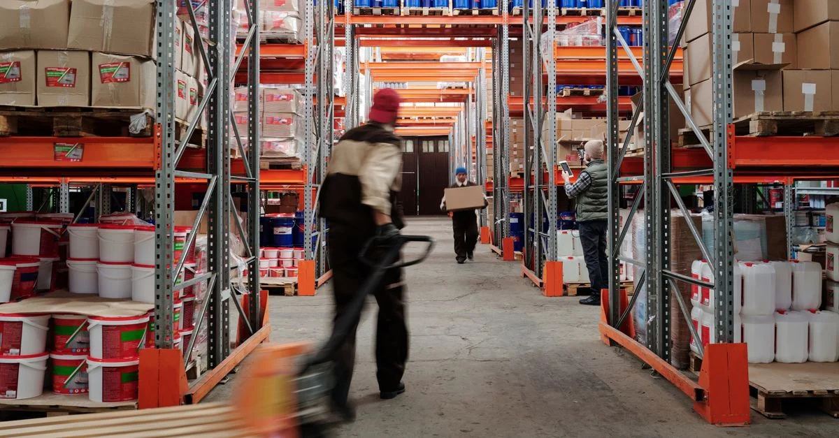 Intérieur d'entrepôt avec des travailleurs organisant des étagères pleines de boîtes et de conteneurs.