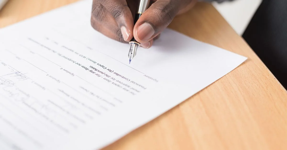Une main tenant un stylo signant un document en gros plan sur un bureau, symbolisant un accord ou la finalisation d'un contrat.