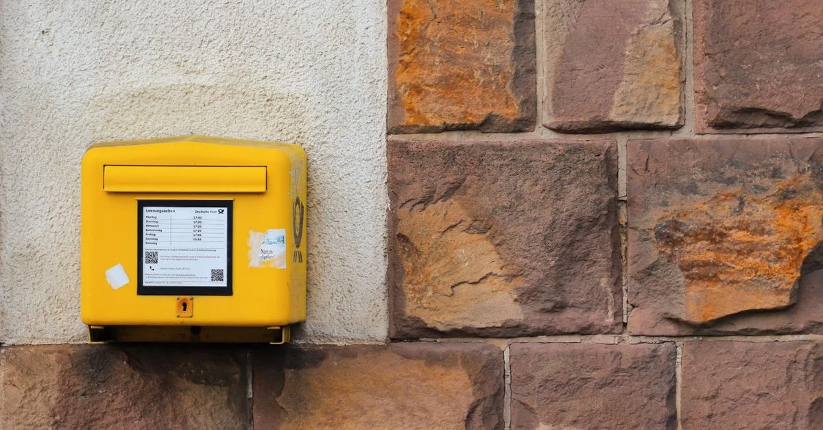 Une boîte aux lettres jaune montée sur un mur de pierre rustique, affichant des informations postales.