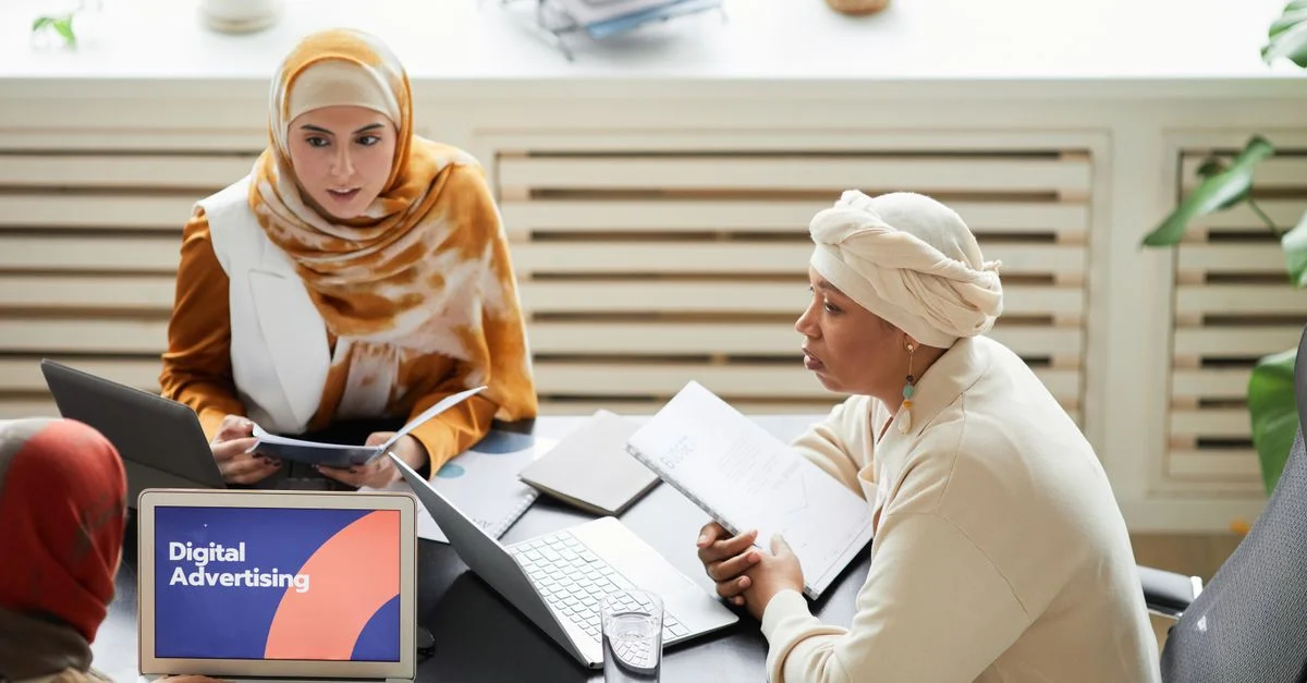 Trois femmes en hijabs collaborant sur des stratégies de publicité numérique autour d'une table avec des ordinateurs portables.