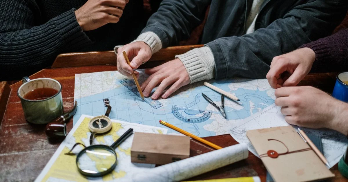 Des adultes planifiant un voyage nautique à l'aide de cartes, boussoles et outils à l'intérieur.