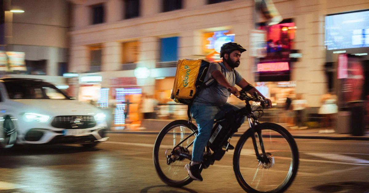 Un livreur de nourriture à vélo traverse les rues animées de Madrid la nuit.