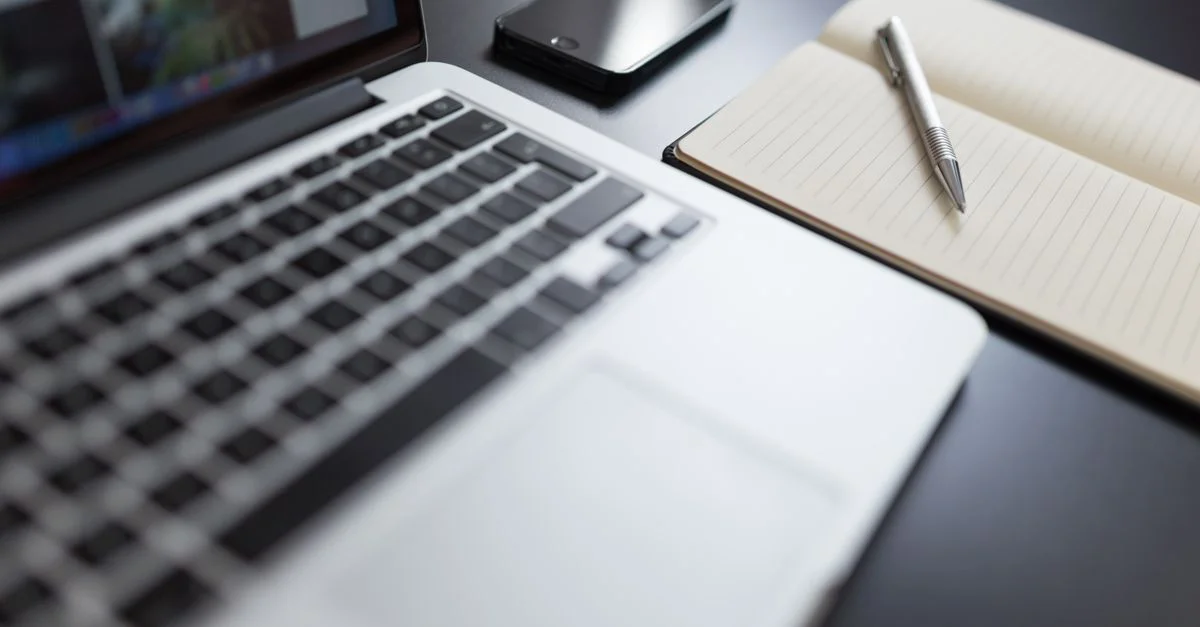 Un espace de travail moderne avec un ordinateur portable, un carnet, un smartphone et un stylo sur un bureau.