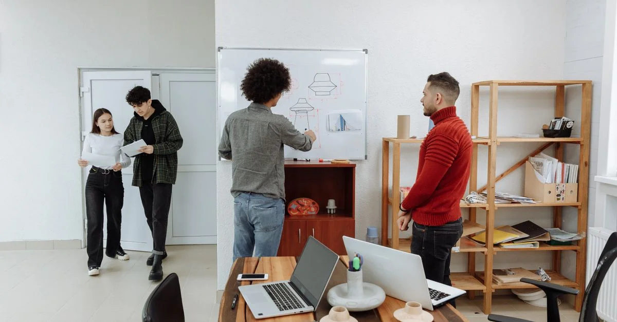 Équipe diversifiée collaborant dans un bureau moderne, discutant d'idées avec des ordinateurs portables et un tableau blanc.