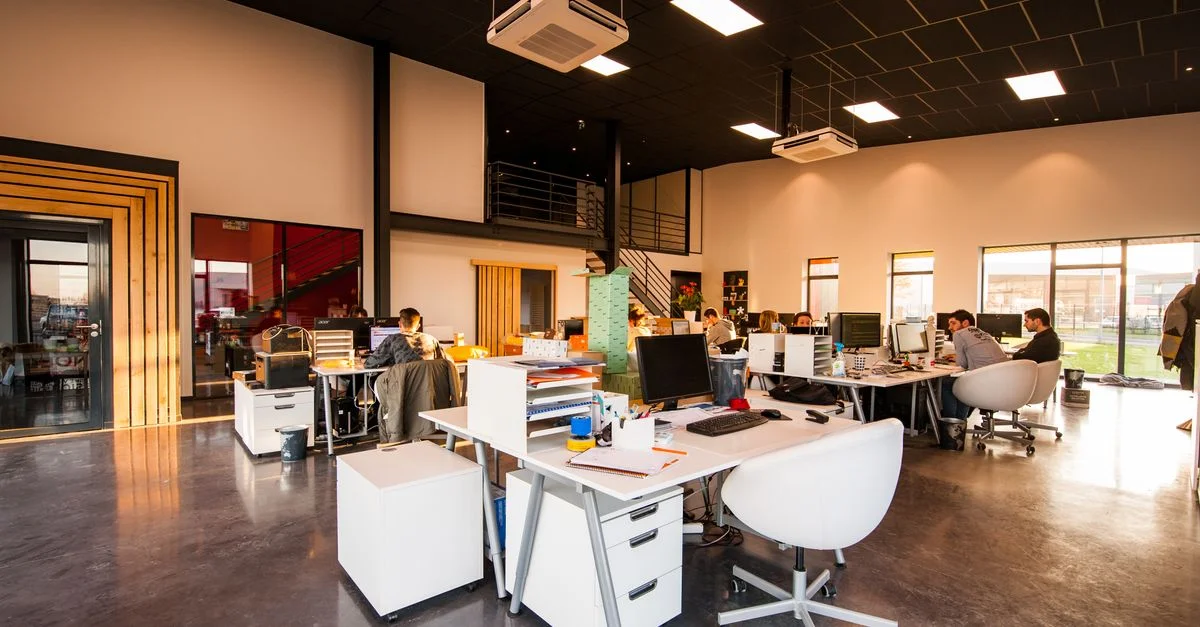 Un bureau moderne et spacieux en open space avec un éclairage naturel et des employés travaillant à des bureaux.