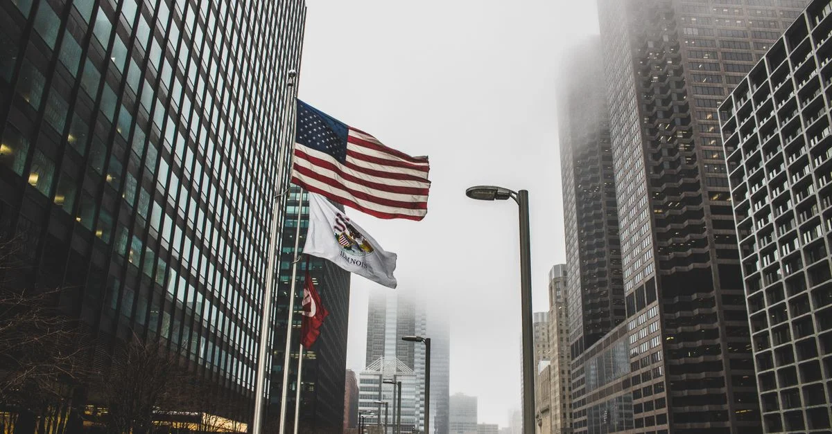 Drapeaux américains flottant dans un paysage urbain brumeux entre des gratte-ciels modernes.