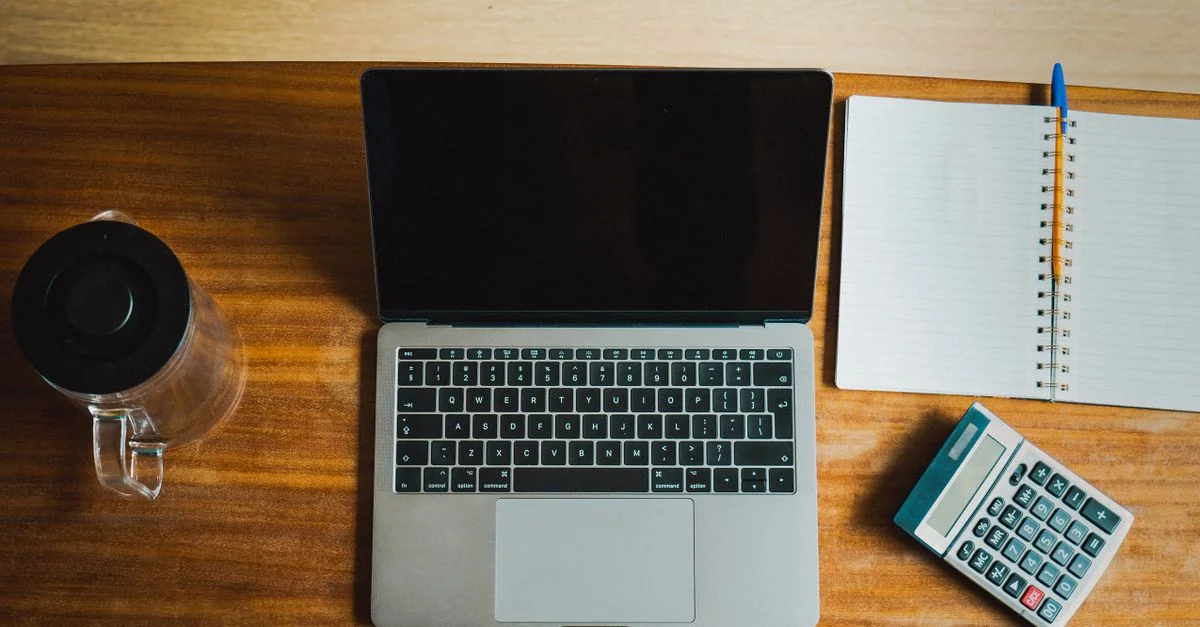 Vue de dessus d'un espace de travail avec un ordinateur portable, une calculatrice et un cahier sur un bureau en bois.