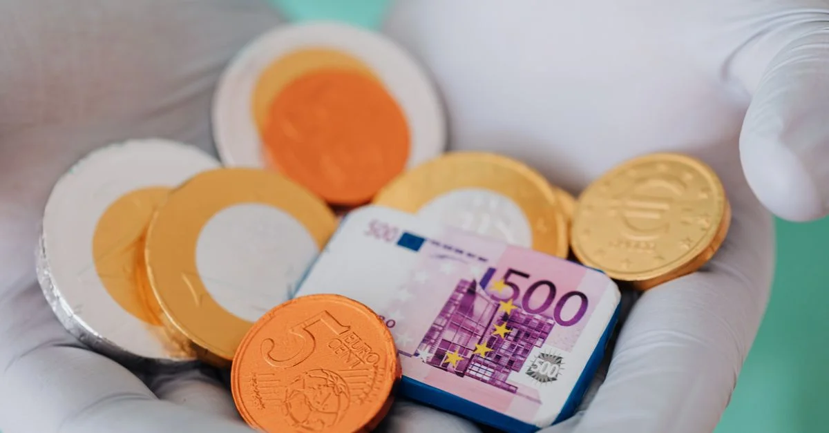 Une main gantée montrant des pièces en chocolat et un billet en euros.