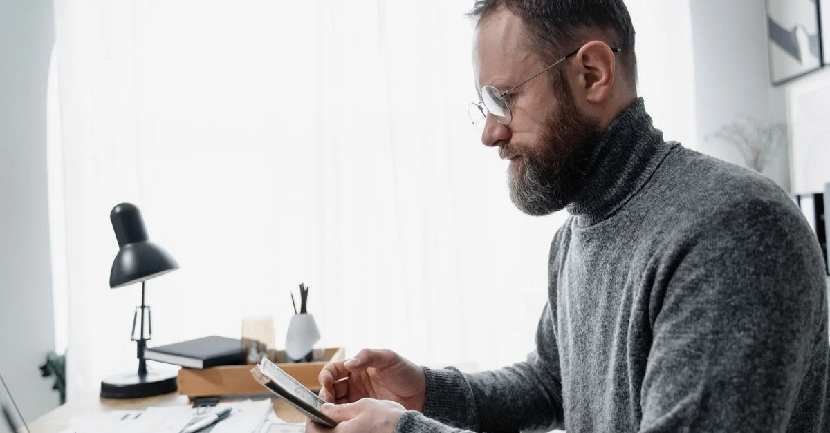 Homme adulte révisant des documents à un bureau avec un aménagement moderne, transmettant concentration et attention.