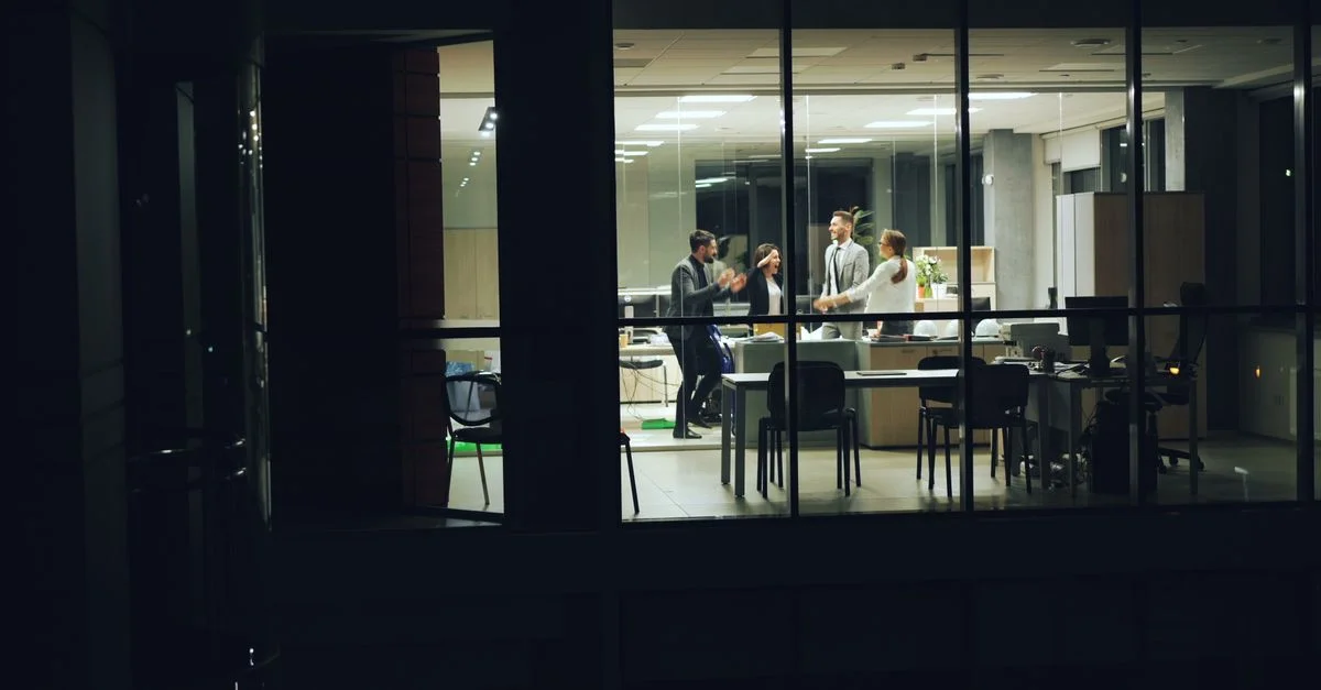 Équipe d'affaires célébrant le succès dans un bureau en verre moderne la nuit.