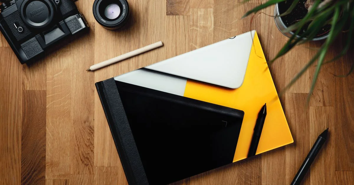 Un espace de travail créatif avec un appareil photo, des fournitures de bureau et une plante sur un bureau en bois vu de dessus.