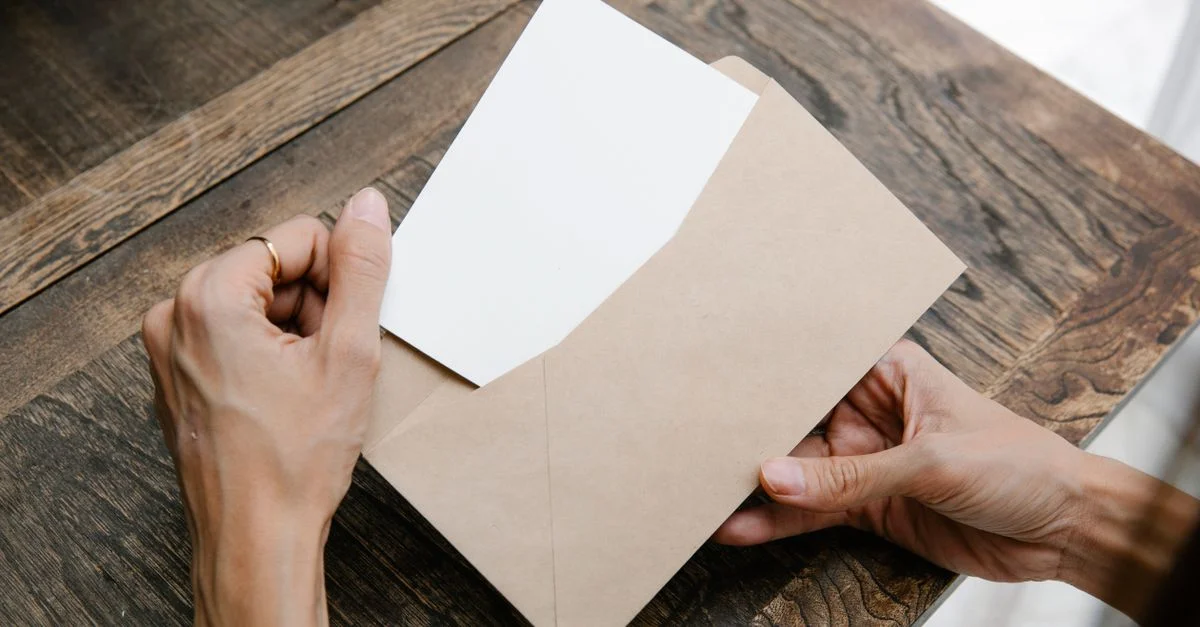 Des mains tenant une lettre à l'intérieur d'une enveloppe marron sur un bureau en bois, vue de dessus.