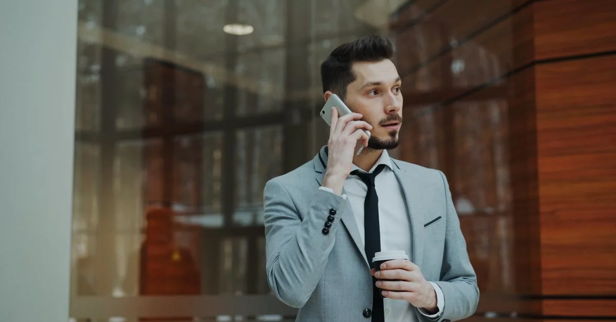 Homme d'affaires confiant en costume gris conversant sur un smartphone à l'intérieur.