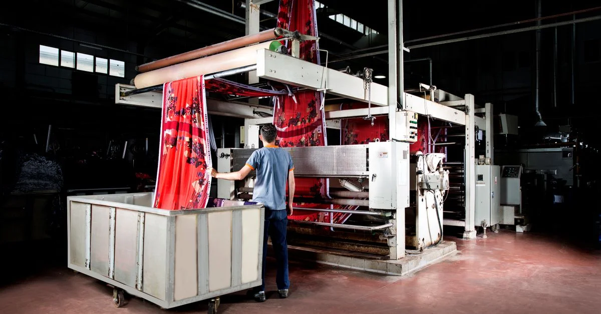 Un travailleur opère des machines dans une usine textile, supervisant la production de tissu.