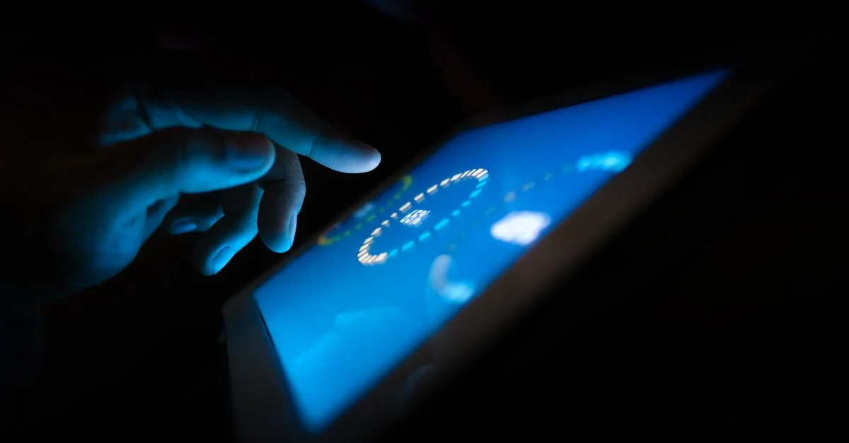 Gros plan sur une main interagissant avec un écran tactile lumineux dans un environnement sombre, mettant en avant l'utilisation de la technologie.