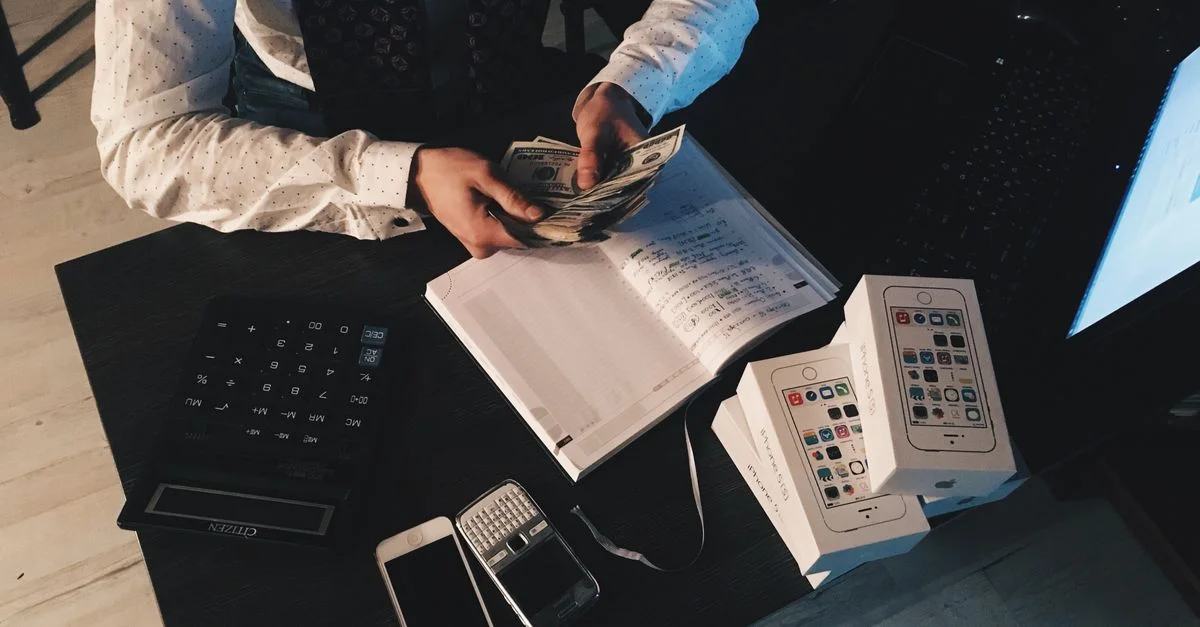 Homme d'affaires organisant ses finances avec des appareils technologiques et de l'argent sur le bureau.