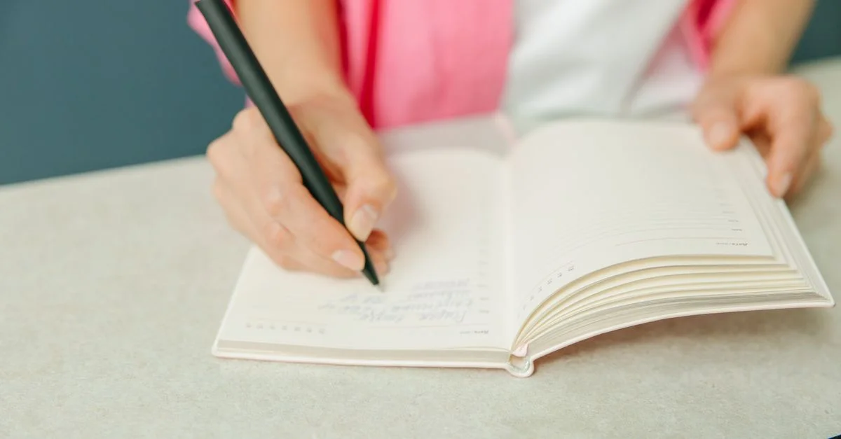 Gros plan sur une personne prenant des notes dans un planner sur un bureau. Idéal pour des thèmes de productivité.