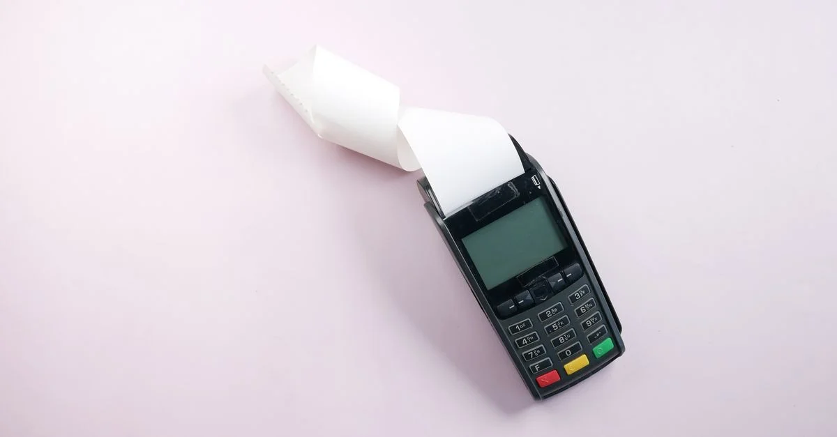 Vue de dessus d'un terminal de paiement avec un reçu sur un fond rose clair. Parfait pour du contenu lié à la finance.