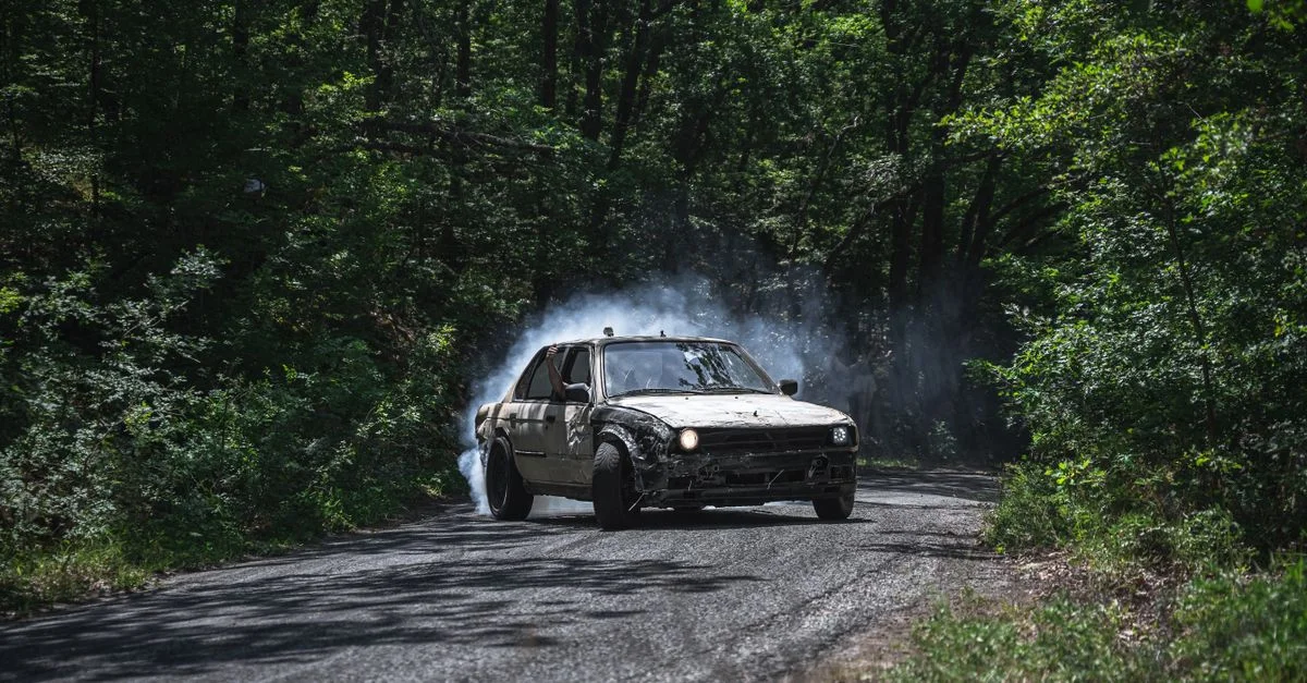 Une voiture classique dérivant sur une route en asfalt entourée d'une dense forêt verte.