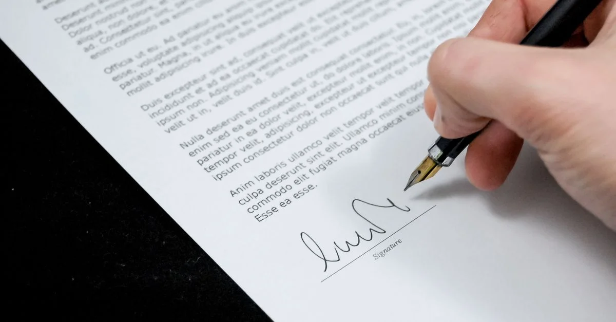Gros plan sur une main signant un document formel avec un stylo plume, indiquant un accord.