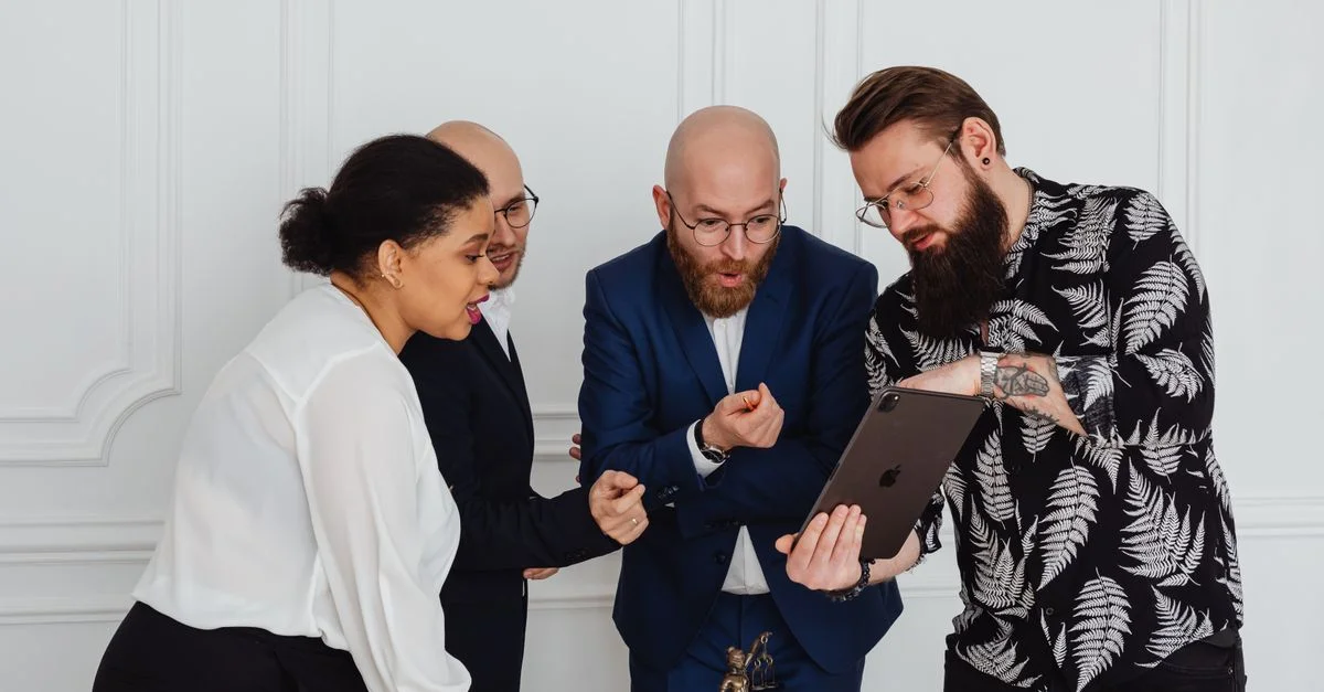 Équipe diverse rassemblée autour d'une tablette dans un environnement de bureau moderne, engagée dans une discussion.