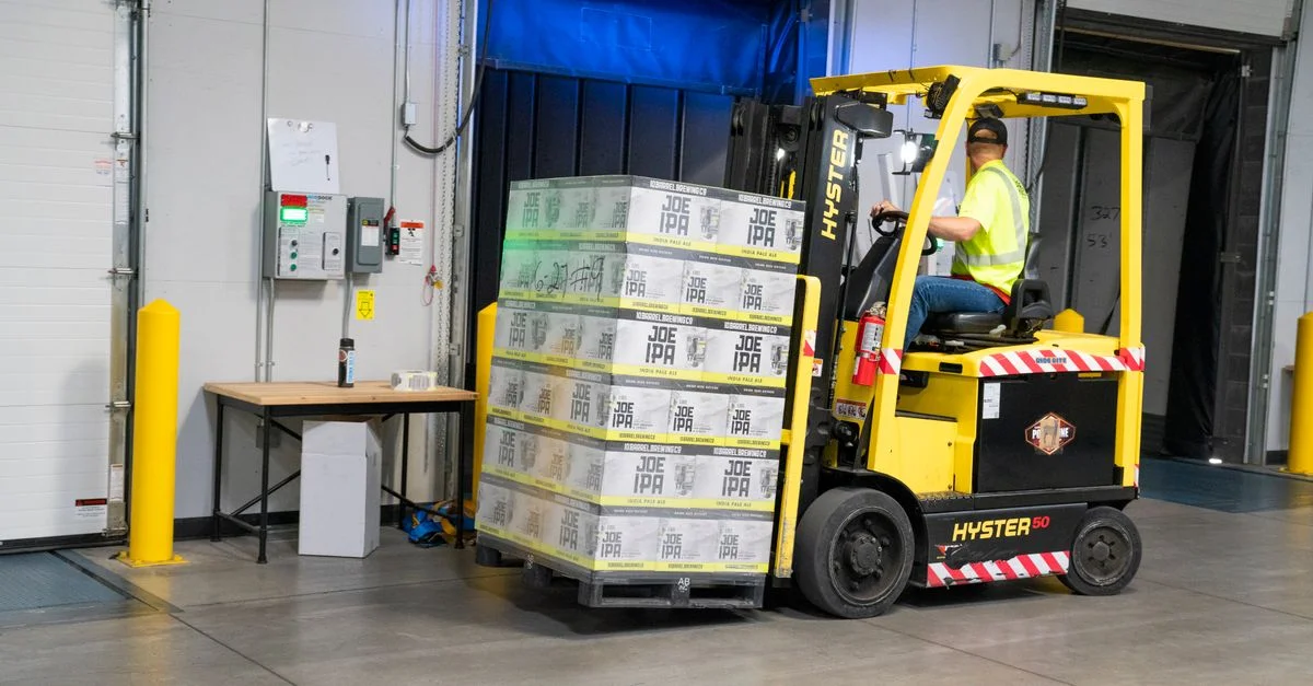 Un employé d'entrepôt manœuvrant un chariot élévateur pour déplacer des marchandises stockées à l'intérieur. Parfait pour des visuels sur l'industrie et la logistique.