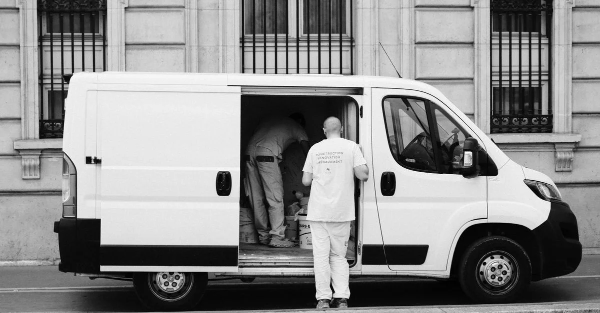 Image monochrome d'une camionnette de livraison avec des travailleurs, mettant en avant la logistique urbaine.