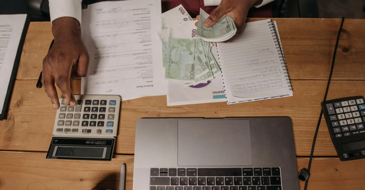 Gros plan sur une personne comptant des espèces avec des documents et un ordinateur portable dans un bureau.