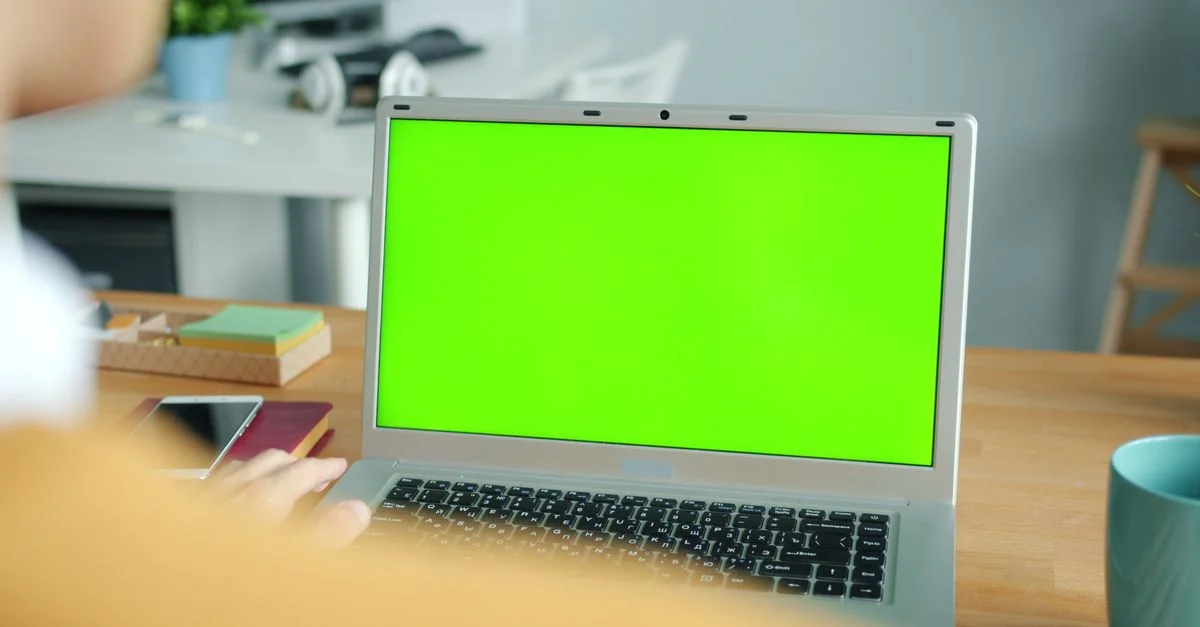 Personne travaillant sur un ordinateur portable avec un écran vert dans un bureau moderne.