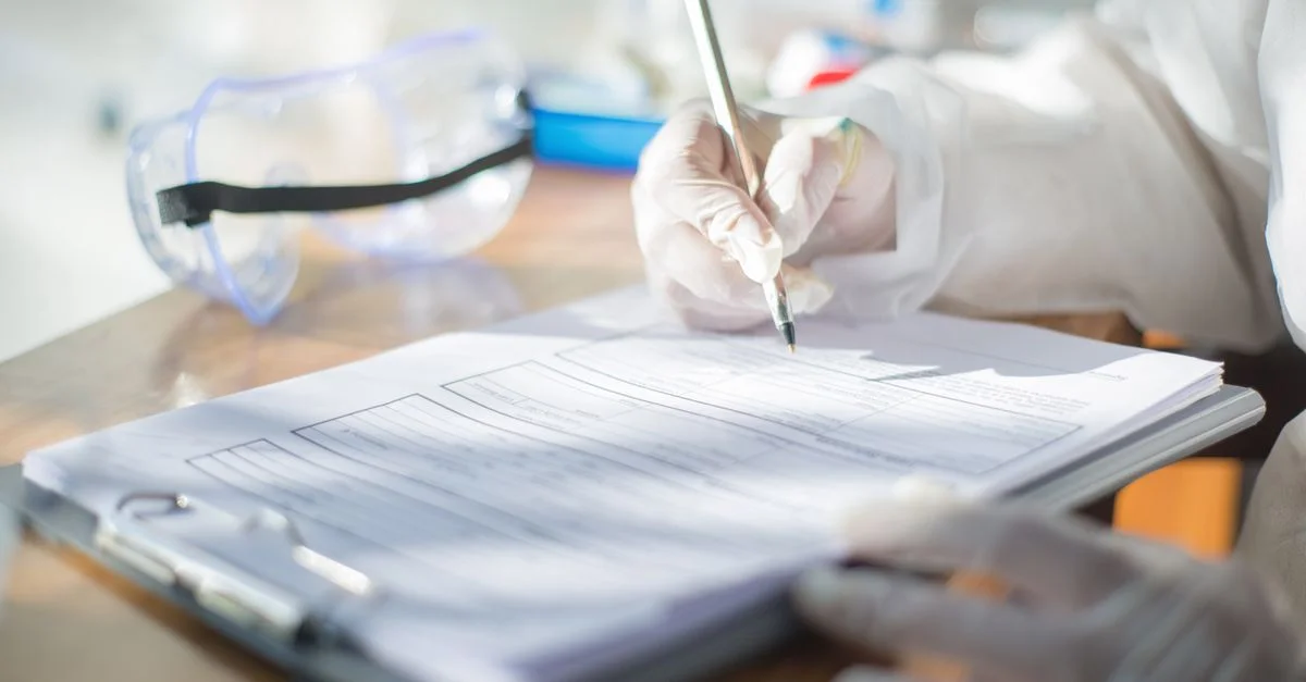 Gros plan d'un scientifique écrivant sur un document avec des gants dans un cadre de laboratoire.