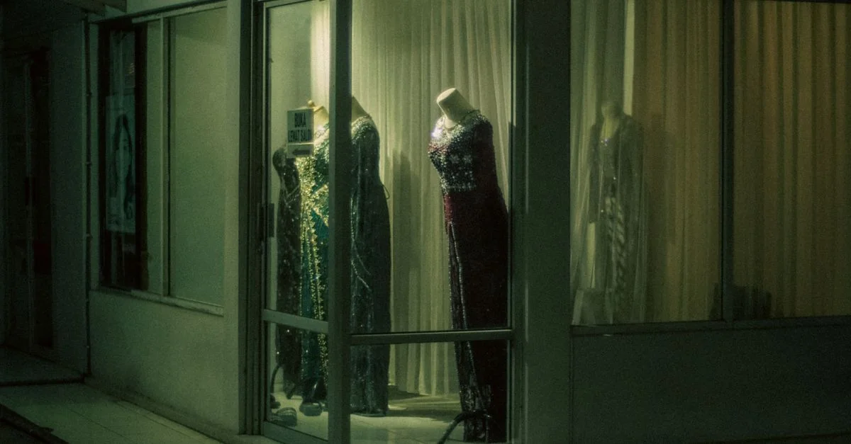 Vitrine présentant des robes de soirée glorieuses sous un éclairage nocturne doux.