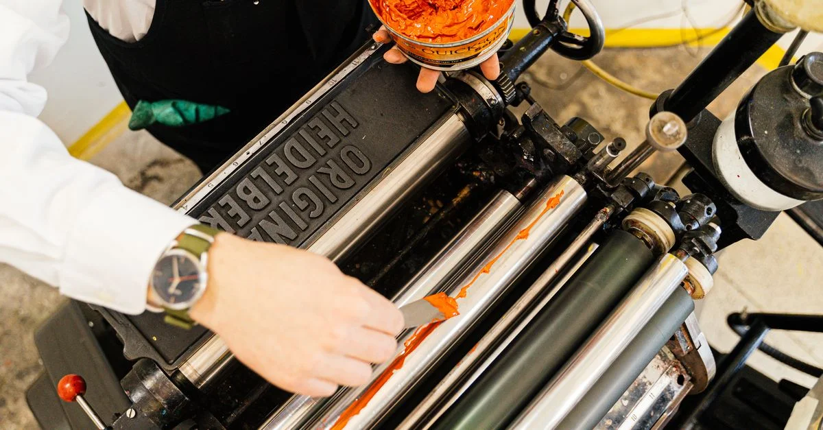 Une personne appliquant de l'encre sur une presse d'impression Heidelberg vintage dans un atelier.
