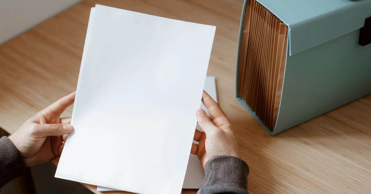 Des mains tenant une feuille de papier vierge à côté d'une boîte de rangement turquoise sur un bureau en bois.